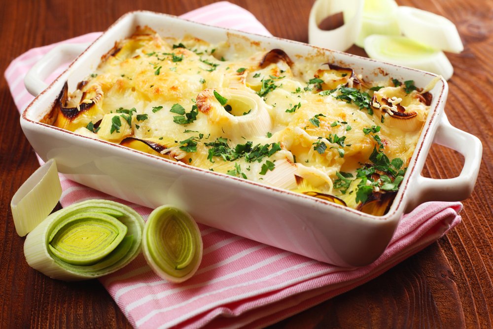 Gratinado de alho-poró e bacon servido em um prato branco, decorado com salsinha