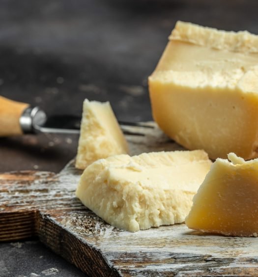Queijo gruyère cortado em pedaços sobre uma tábua de madeira, mostrando sua textura e versatilidade para diferentes pratos.