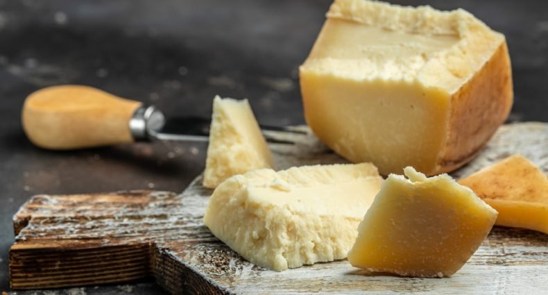 Queijo gruyère cortado em pedaços sobre uma tábua de madeira, mostrando sua textura e versatilidade para diferentes pratos.