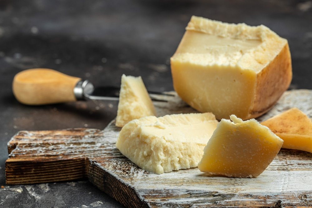 Queijo gruyère cortado em pedaços sobre uma tábua de madeira, mostrando sua textura e versatilidade para diferentes pratos.