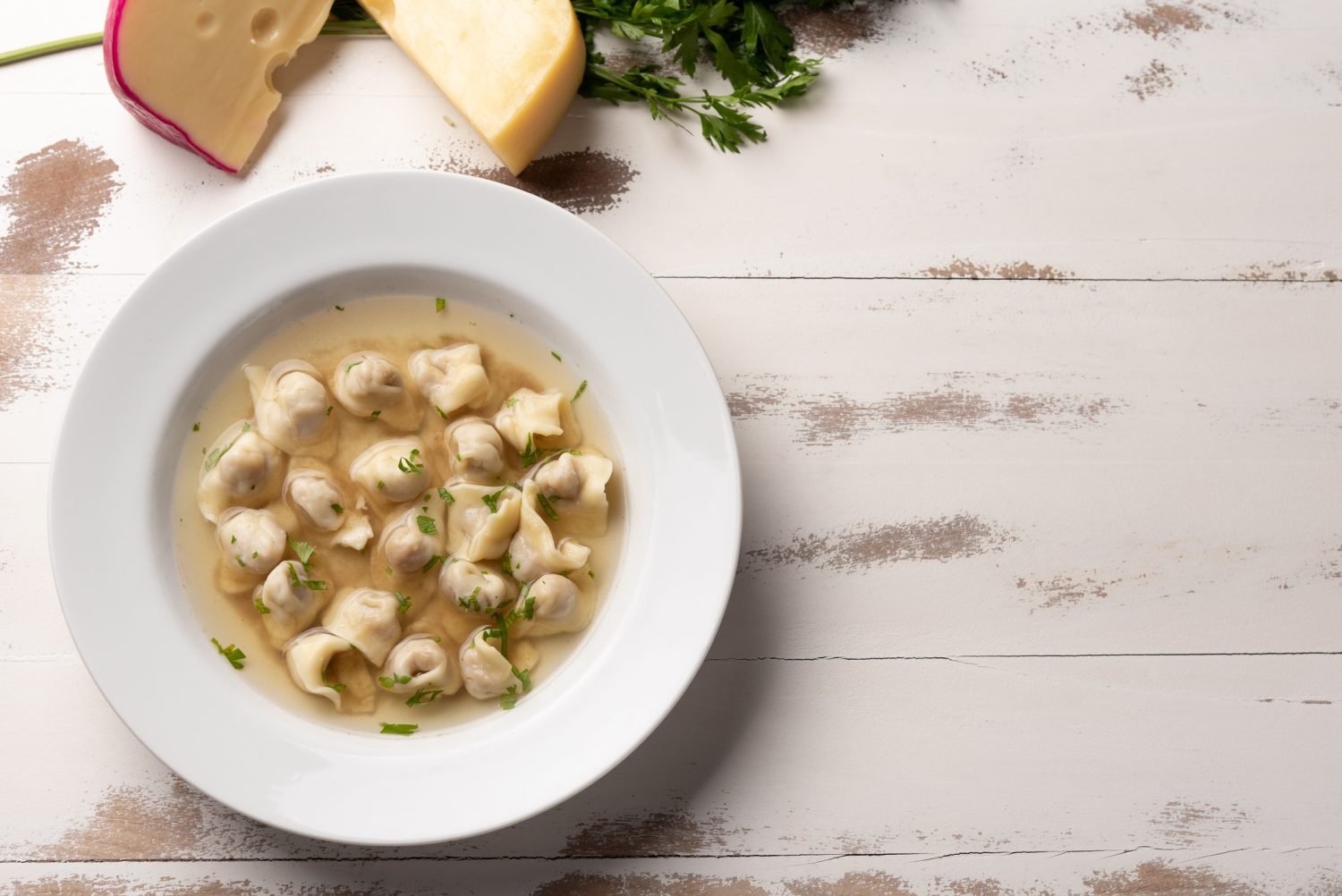 Sopa de capeletti em prato branco com ervas.