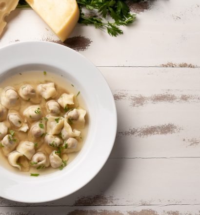 Sopa de capeletti em prato branco com ervas.