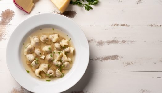 Sopa de capeletti em prato branco com ervas.