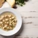 Sopa de capeletti em prato branco com ervas.