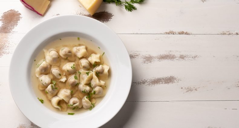 Sopa de capeletti em prato branco com ervas.