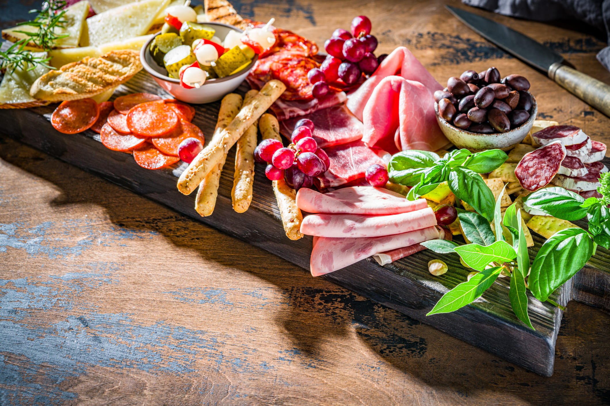 Tábua de charcutaria com diversos produtos, acompanhada de frutas e picles.