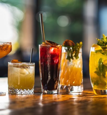 Cinco diferentes copos e taças apresentados com cocktails variados em um ambiente iluminado