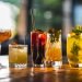 Cinco diferentes copos e taças apresentados com cocktails variados em um ambiente iluminado
