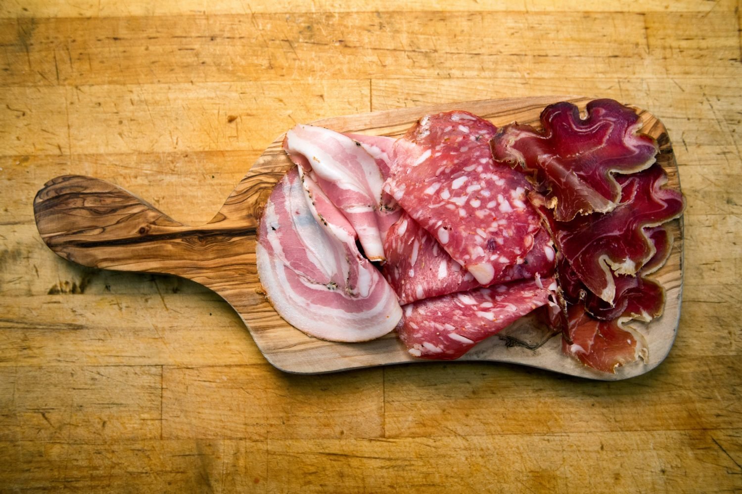 Placa de madeira com diferentes tipos de charcutaria, incluindo presunto e salame.
