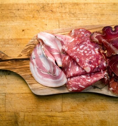 Placa de madeira com diferentes tipos de charcutaria, incluindo presunto e salame.