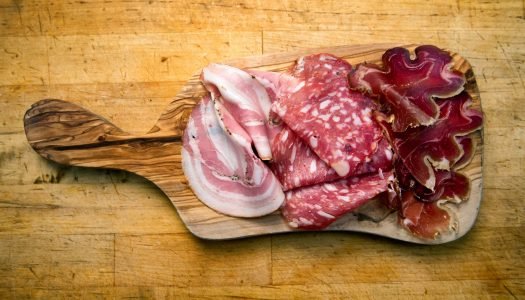 Placa de madeira com diferentes tipos de charcutaria, incluindo presunto e salame.