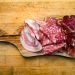 Placa de madeira com diferentes tipos de charcutaria, incluindo presunto e salame.