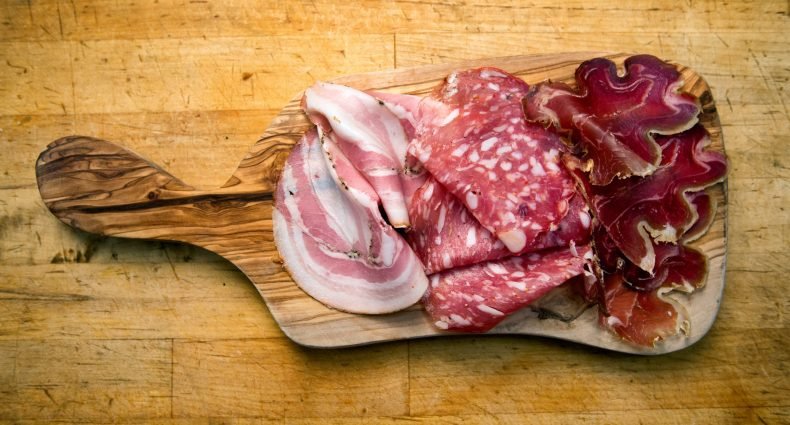 Placa de madeira com diferentes tipos de charcutaria, incluindo presunto e salame.