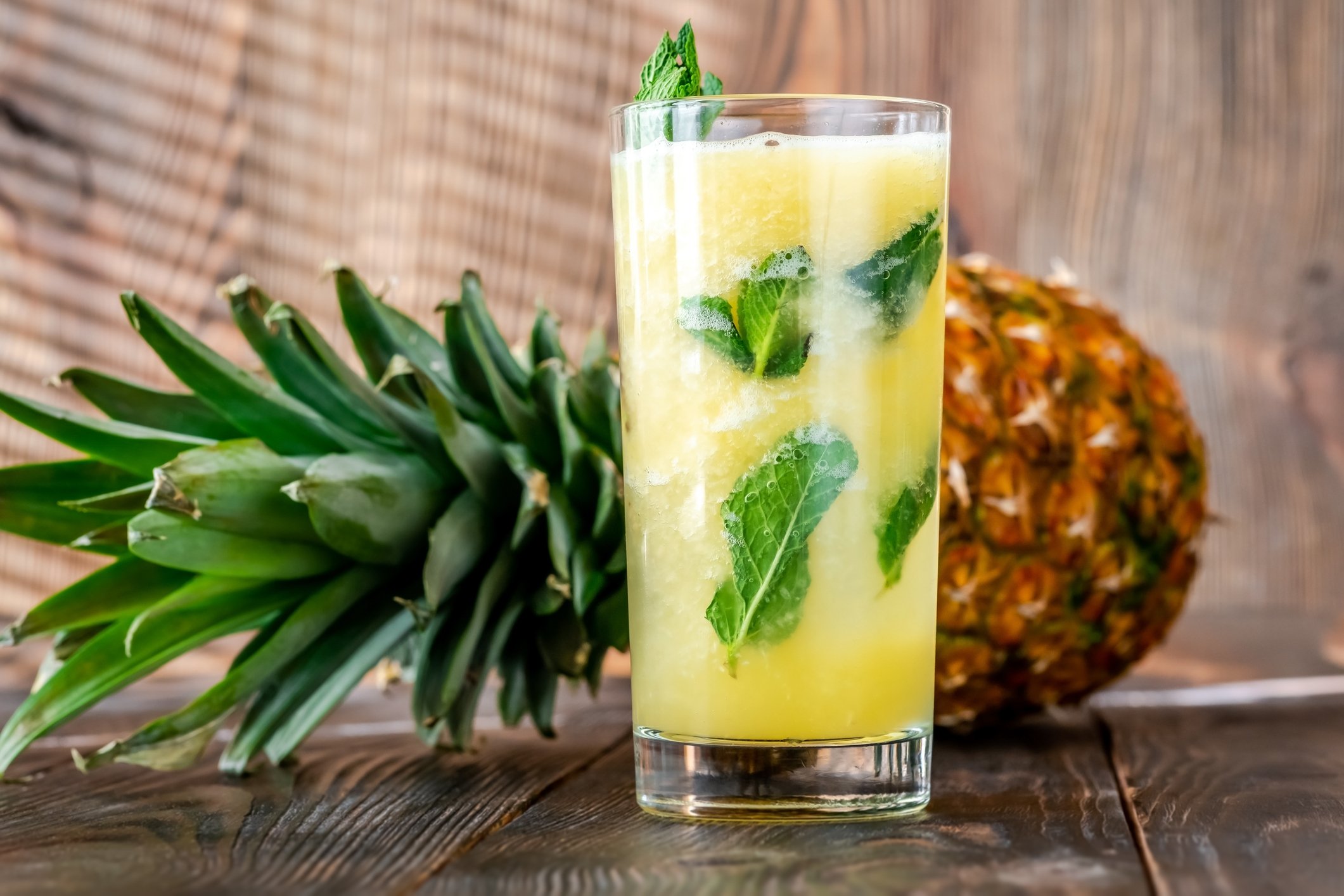Caipirinha de abacaxi com hortelã em copo alto ao lado de abacaxi fresco