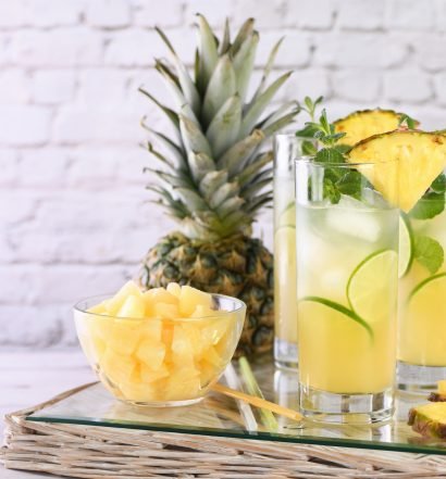 Caipirinha de abacaxi com fatias e cubos de abacaxi em copos altos