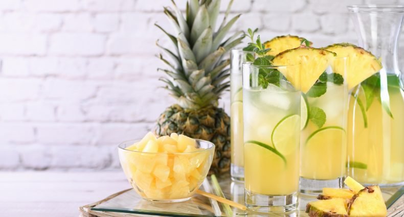 Caipirinha de abacaxi com fatias e cubos de abacaxi em copos altos
