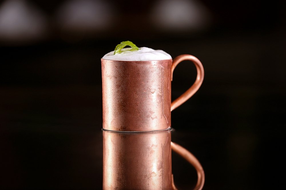 Caneca de cobre com espuma de gengibre decorada com folhas de hortelã, criando uma bebida sofisticada e refrescante.