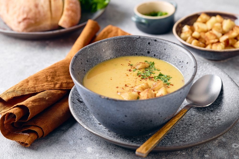 Colher de sopa ao lado de uma tigela de sopa cremosa.