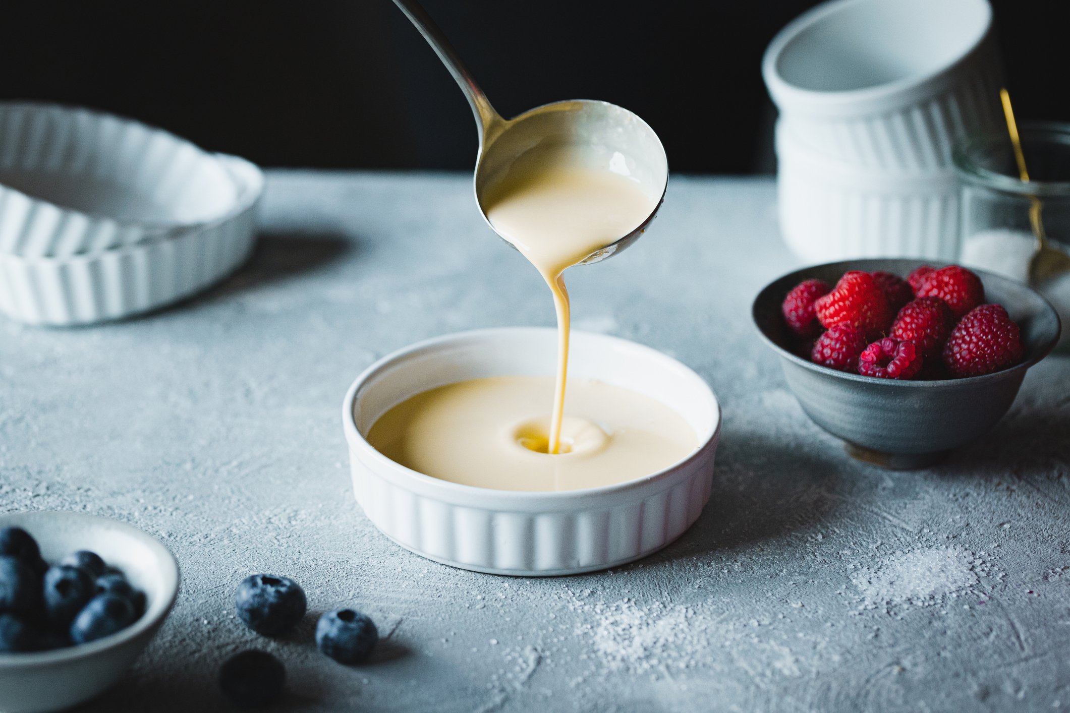 Concha de cozinha servindo creme em ramequim com frutas ao fundo