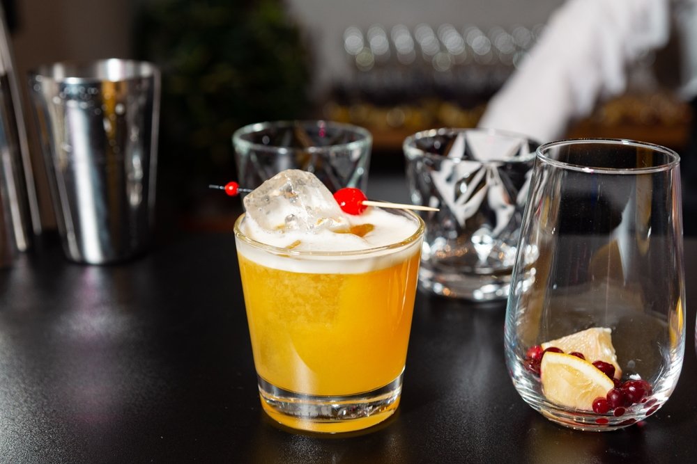 Drink Whisky Sour decorado com laranja e cereja em um copo.