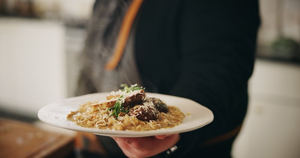 Prato de risoto de funghi servido no ponto certo sendo oferecido