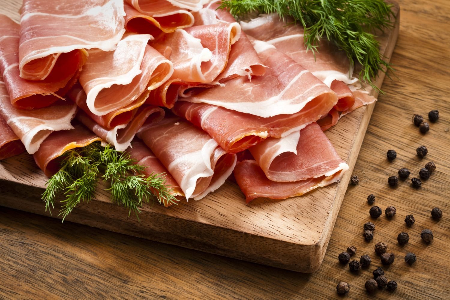 Fatias de presunto parma em tábua de madeira com temperos naturais