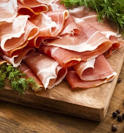 Fatias de presunto parma em tábua de madeira com temperos naturais