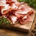 Fatias de presunto parma em tábua de madeira com temperos naturais