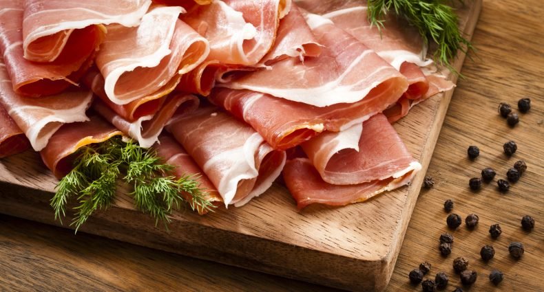 Fatias de presunto parma em tábua de madeira com temperos naturais