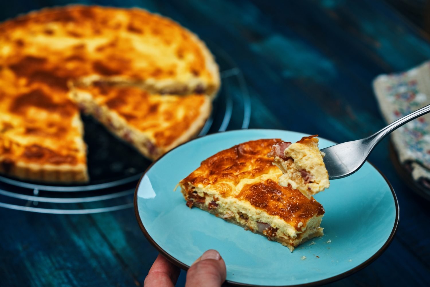Fatia de Quiche Lorraine com crosta dourada, servida em prato azul.