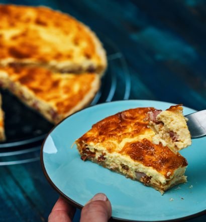Fatia de Quiche Lorraine com crosta dourada, servida em prato azul.
