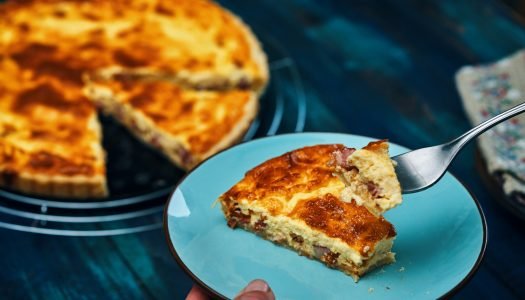 Fatia de Quiche Lorraine com crosta dourada, servida em prato azul.