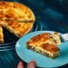Fatia de Quiche Lorraine com crosta dourada, servida em prato azul.