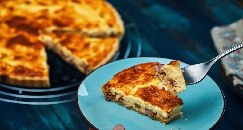Fatia de Quiche Lorraine com crosta dourada, servida em prato azul.