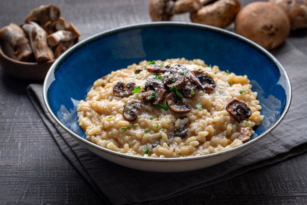 Risoto de funghi cremoso servido em tigela azul com cogumelos salteados por cima