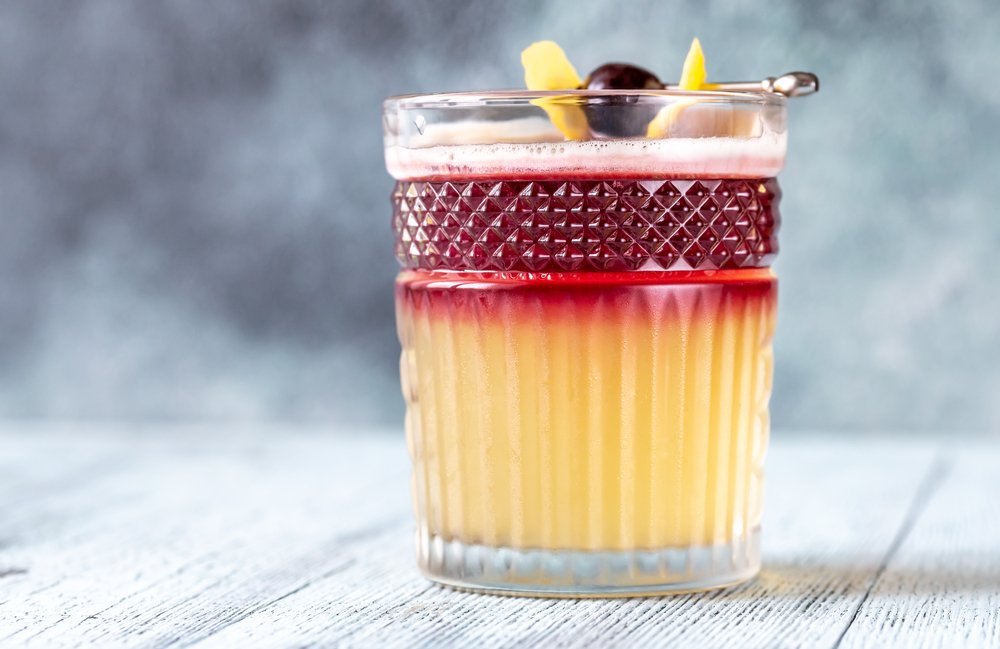 Copo de Whisky Sour com gelo, fatia de limão e cereja no topo.