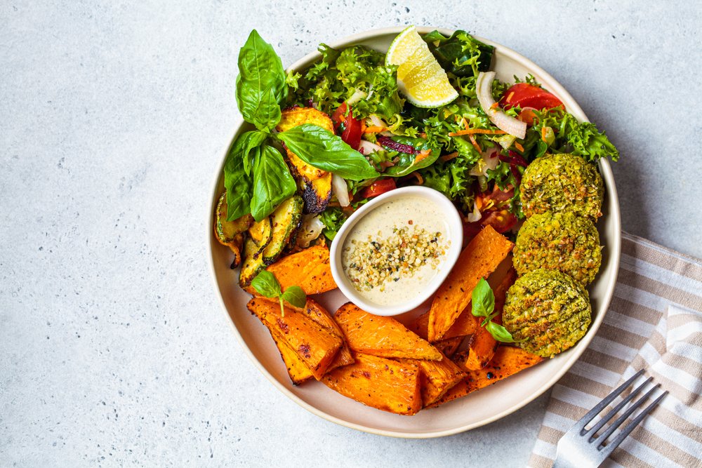 Prato vegano com falafel, batata-doce, salada verde e molho tahine para celebrar o Dia Mundial do Veganismo