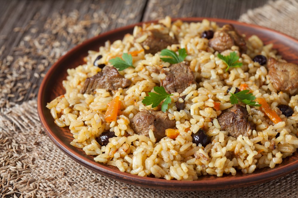 Prato de arroz à grega com carne, passas escuras e cenoura, guarnecido com salsa, representando um acompanhamento saboroso para ocasiões especiais.