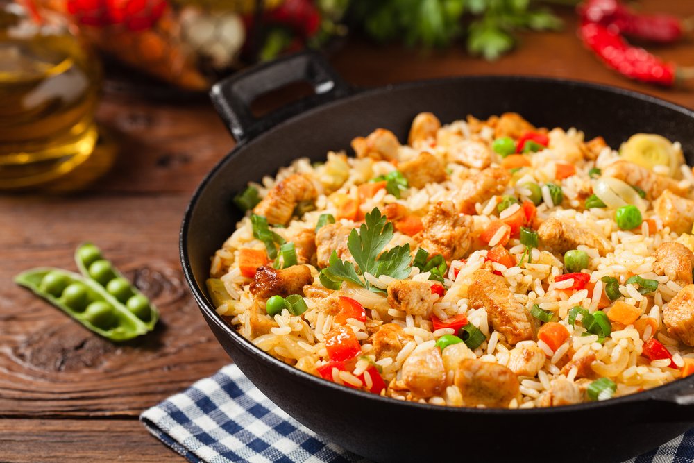 Arroz à grega colorido com frango, ervilhas, cenoura e pimentão em panela preta, ideal para acompanhar refeições festivas.