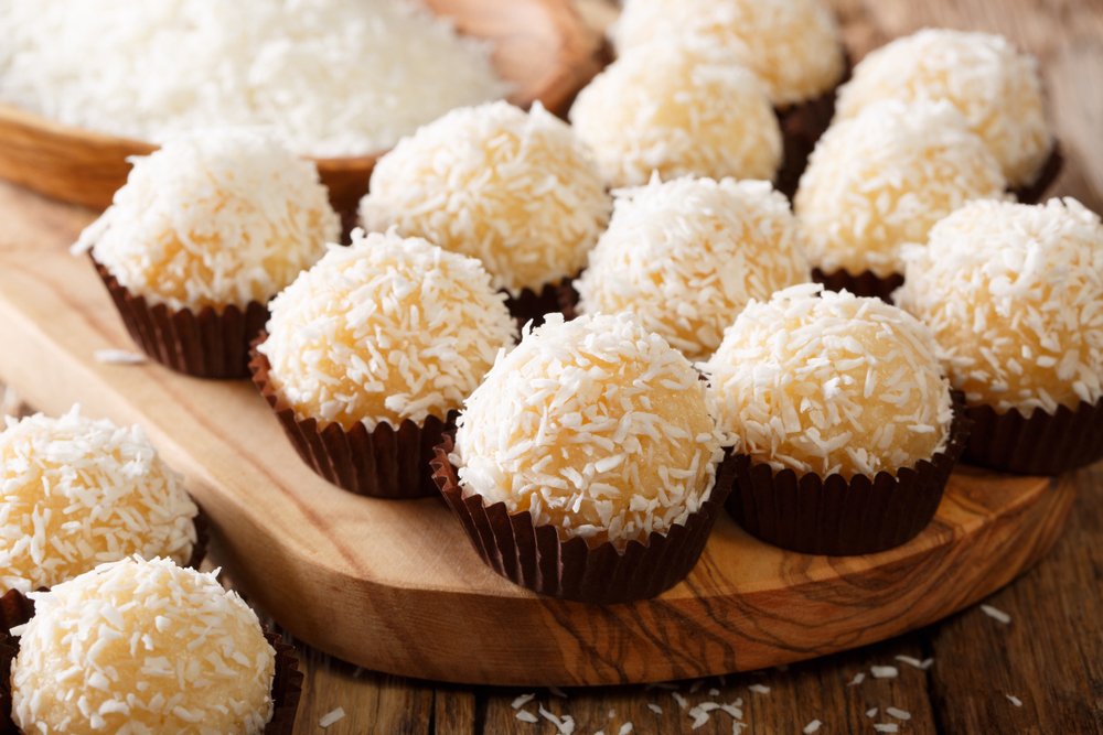 Beijinhos de coco gourmet em forminhas de chocolate, cobertos com coco ralado, perfeitos para festas infantis ou uma sobremesa fácil de fazer com crianças.