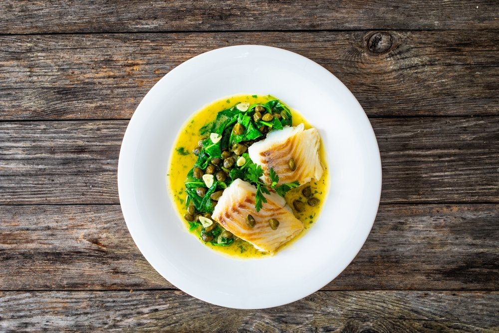 Prato de Belle Meunière com lascas de peixe, espinafre, alcaparras e molho amarelo cremoso