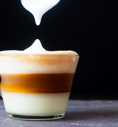 Café cubano com leite, tirado da camada espumosa, com fundo preto.