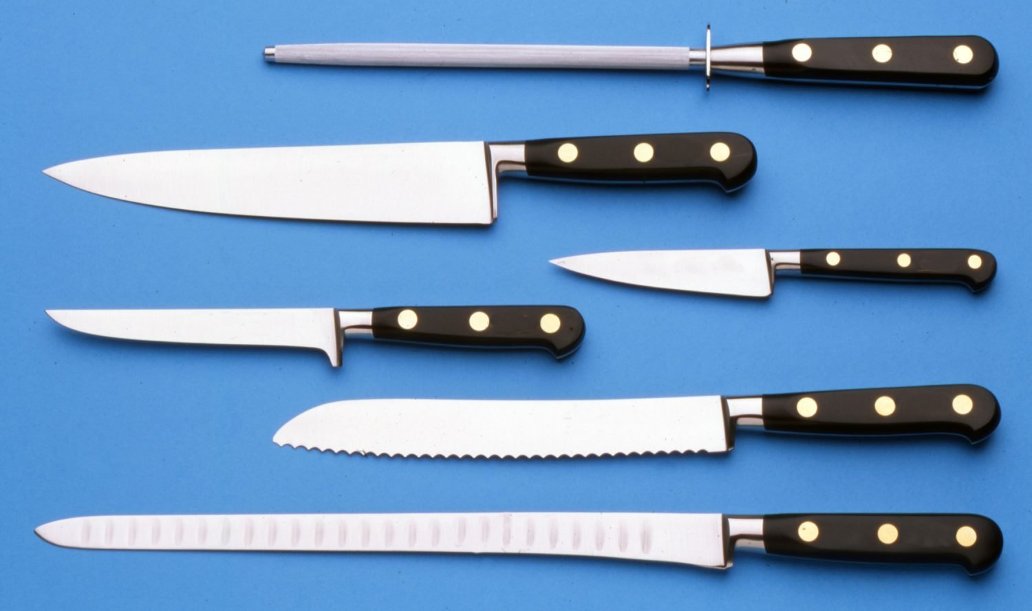 Conjunto de facas de cozinha e chaira sobre fundo azul mostrando diferentes tipos de lâminas