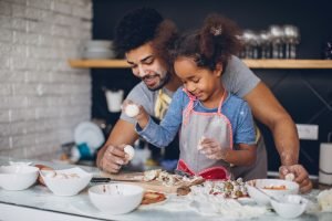 Pai e filha sorrindo, preparando receitas com ovos e farinha na cozinha, aprendendo a cozinhar juntos e se divertindo.