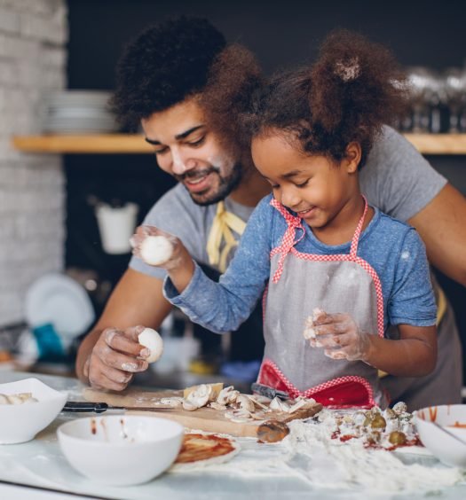 Pai e filha sorrindo, preparando receitas com ovos e farinha na cozinha, aprendendo a cozinhar juntos e se divertindo.