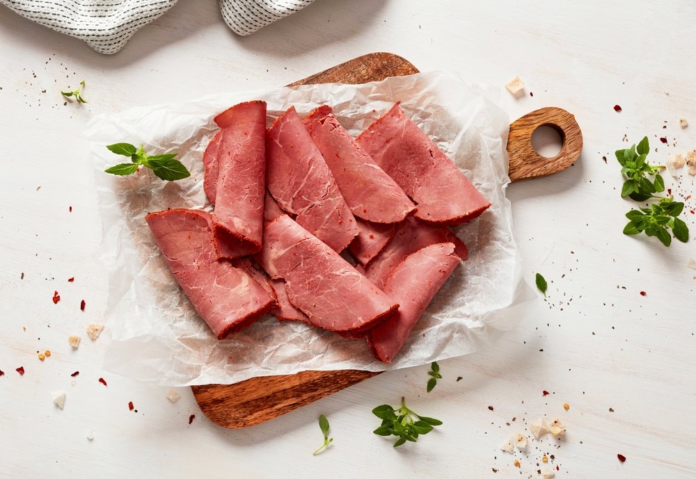 Pastrami fatiado e dobrado artisticamente sobre papel manteiga em tábua de servir, pronto para preparo