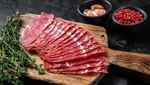 Fatias de pastrami gourmet fresco em tábua de madeira com tomilho e especiarias, ideal para receitas