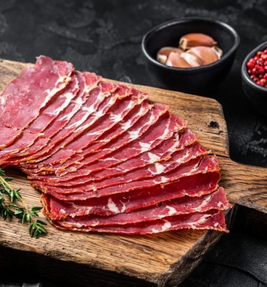 Fatias de pastrami gourmet fresco em tábua de madeira com tomilho e especiarias, ideal para receitas