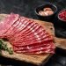 Fatias de pastrami gourmet fresco em tábua de madeira com tomilho e especiarias, ideal para receitas