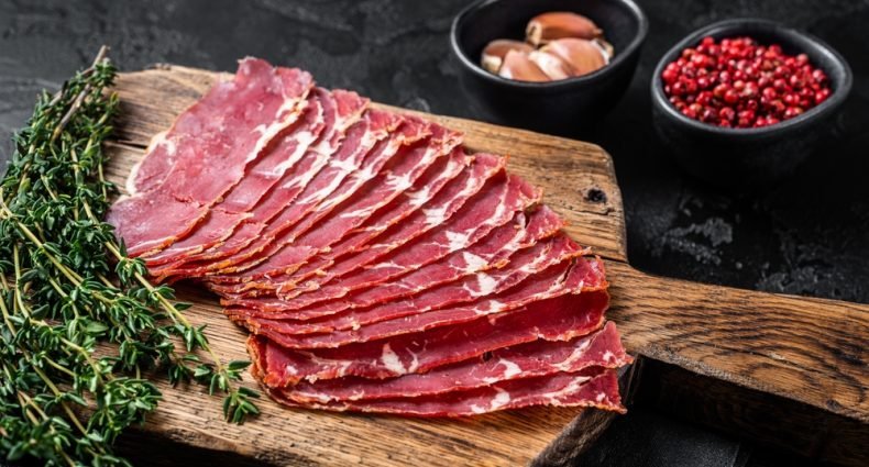 Fatias de pastrami gourmet fresco em tábua de madeira com tomilho e especiarias, ideal para receitas